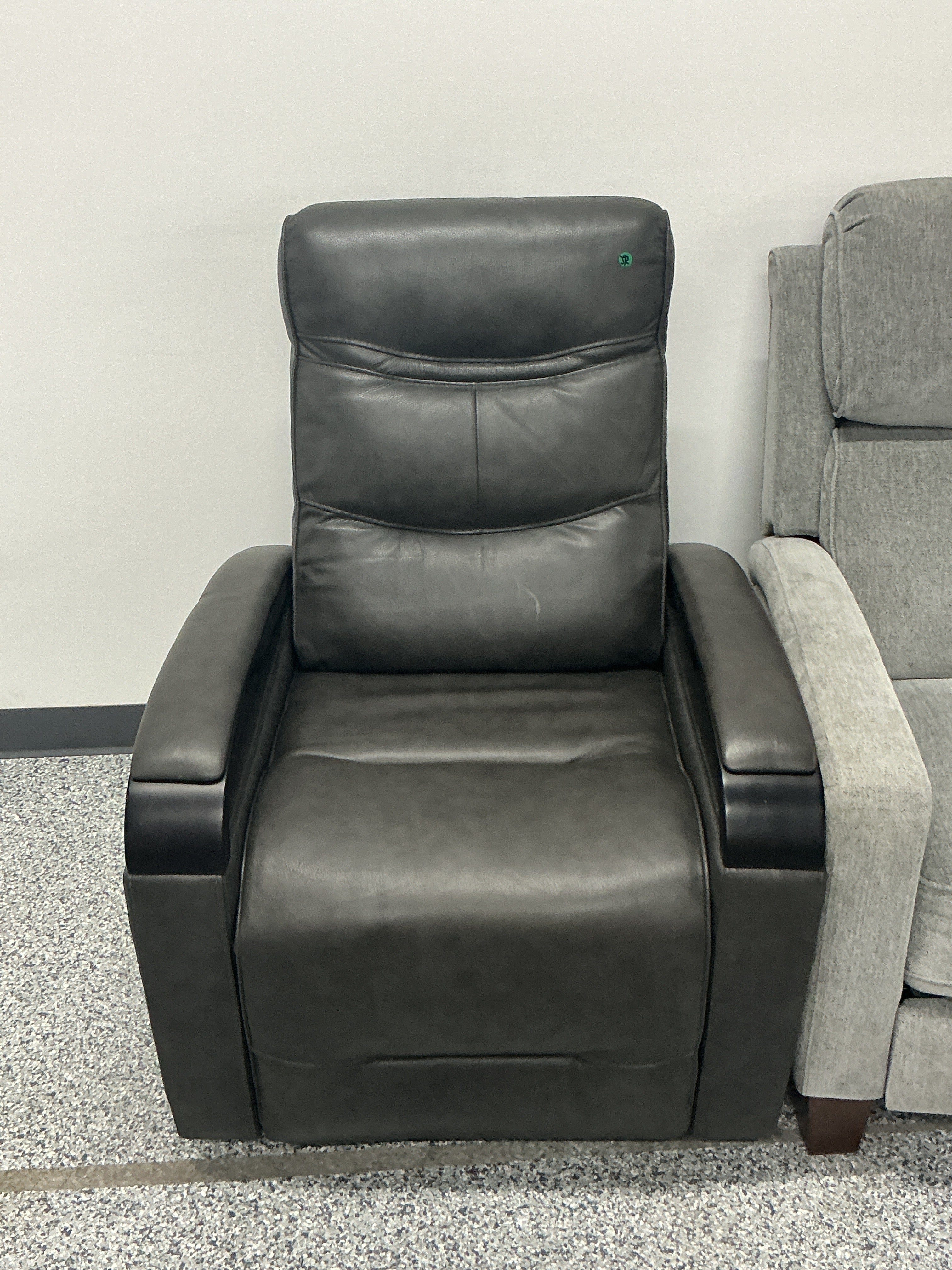 Black leather recliner chair with padded backrest, next to a gray upholstered chair.