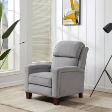 Gray reclining chair with plush upholstery, wood legs, beside a floor lamp and window.